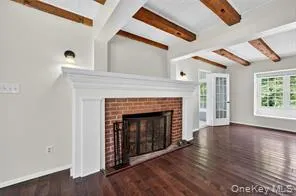 Unfurnished living room with beam ceiling, wood finished floors, and a fireplace Unfurnished living room with beam ceiling, wood finished floors, and a fireplace