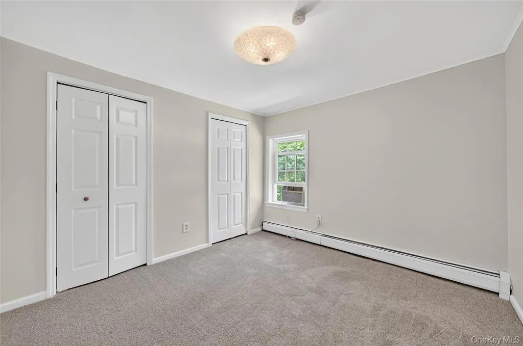 Unfurnished bedroom with a baseboard heating unit, two closets, carpet flooring, and cooling unit Unfurnished bedroom with a baseboard heating unit, two closets, carpet flooring, and cooling unit