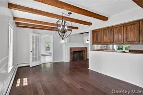 Unfurnished living room featuring a chandelier, dark wood-style flooring, beamed ceiling, a fireplace, and a baseboard heating unit Unfurnished living room featuring a chandelier, dark wood-style flooring, beamed ceiling, a fireplace, and a baseboard heating unit