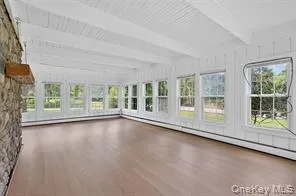 Unfurnished sunroom with wood finished floors, healthy amount of natural light, a baseboard radiator, and beamed ceiling Unfurnished sunroom with wood finished floors, healthy amount of natural light, a baseboard radiator, and beamed ceiling