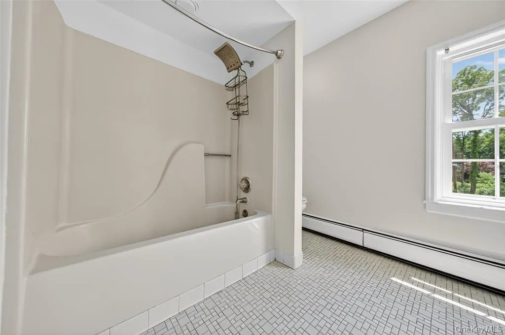 Full bath with healthy amount of natural light,  shower combination, baseboard heating, and tile patterned floors Full bath with healthy amount of natural light,  shower combination, baseboard heating, and tile patterned floors