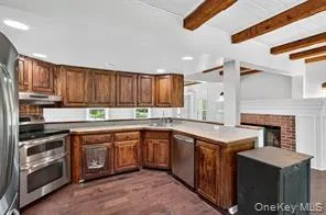 Kitchen with stainless steel appliances, a peninsula, beam ceiling, dark wood finished floors, and brown cabinetry Kitchen with stainless steel appliances, a peninsula, beam ceiling, dark wood finished floors, and brown cabinetry