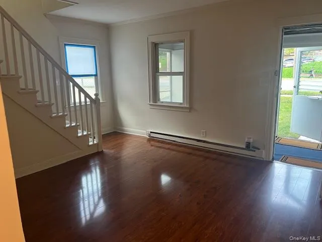 Unfurnished living room featuring stairs, baseboard heating, dark wood-style floors, and ornamental molding Unfurnished living room featuring stairs, baseboard heating, dark wood-style floors, and ornamental molding
