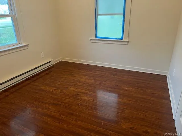 Unfurnished room with dark wood-style floors and baseboard heating Unfurnished room with dark wood-style floors and baseboard heating