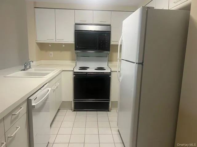 Kitchen featuring white appliances, light countertops, light tile patterned floors, and white cabinetry Kitchen featuring white appliances, light countertops, light tile patterned floors, and white cabinetry