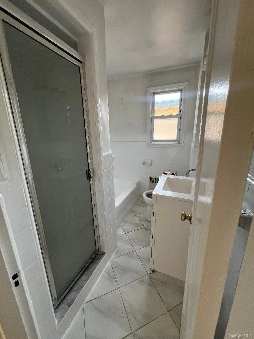 Bathroom featuring vanity, tile walls, a shower stall, a bath, and radiator Bathroom featuring vanity, tile walls, a shower stall, a bath, and radiator