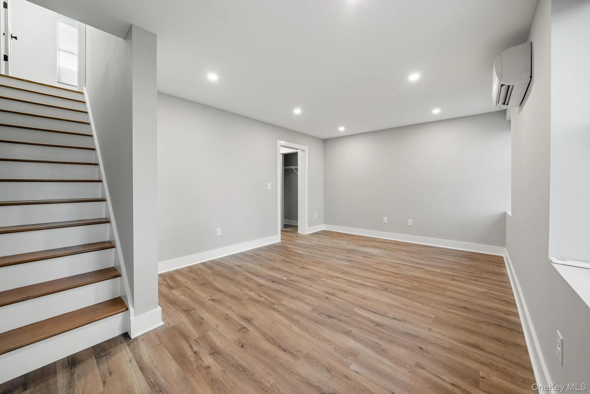 Below grade area featuring recessed lighting, light wood-style flooring, stairs, and a wall mounted AC Below grade area featuring recessed lighting, light wood-style flooring, stairs, and a wall mounted AC