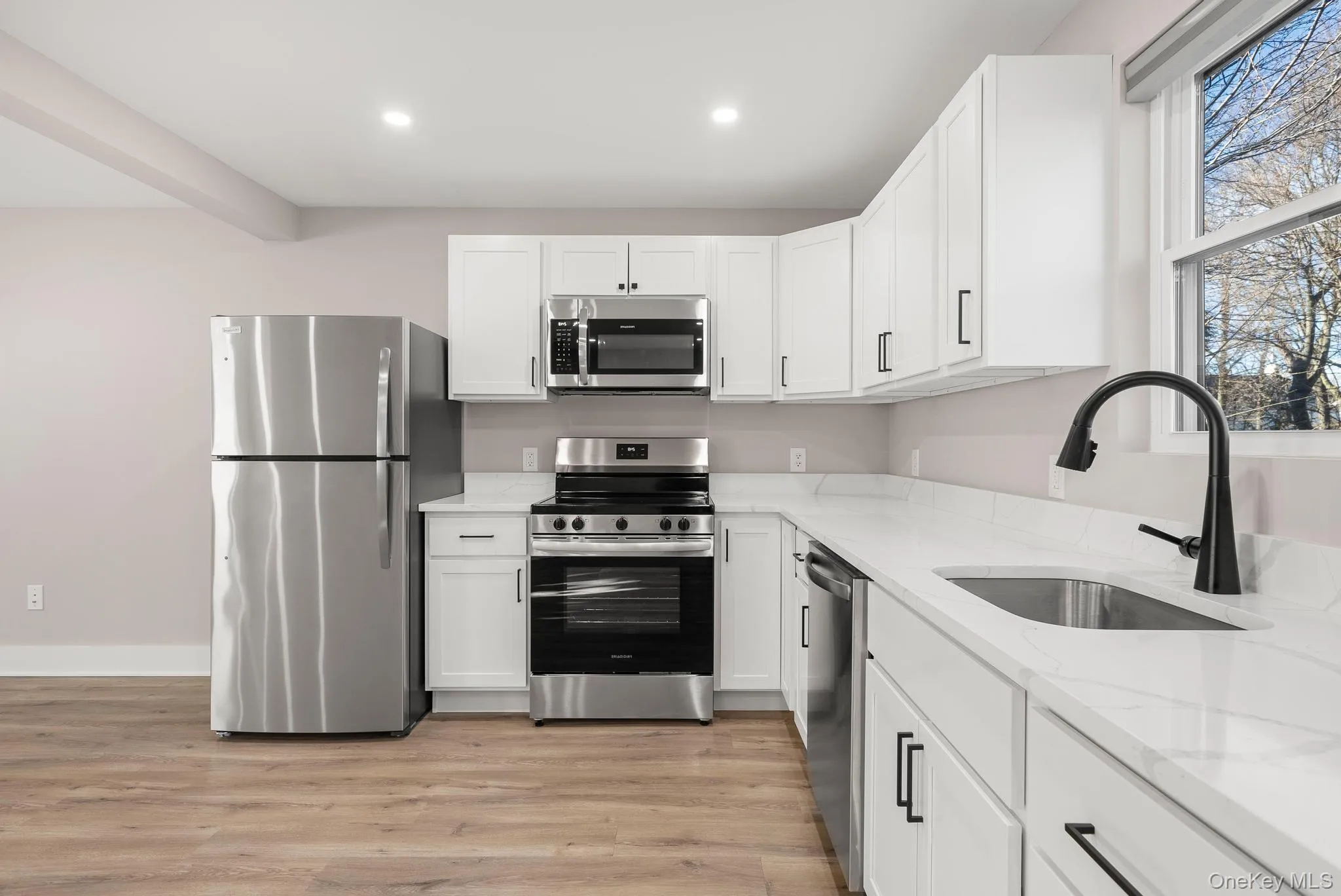 Kitchen with stainless steel appliances, light stone countertops, light wood-type flooring, white cabinets, and recessed lighting Kitchen with stainless steel appliances, light stone countertops, light wood-type flooring, white cabinets, and recessed lighting