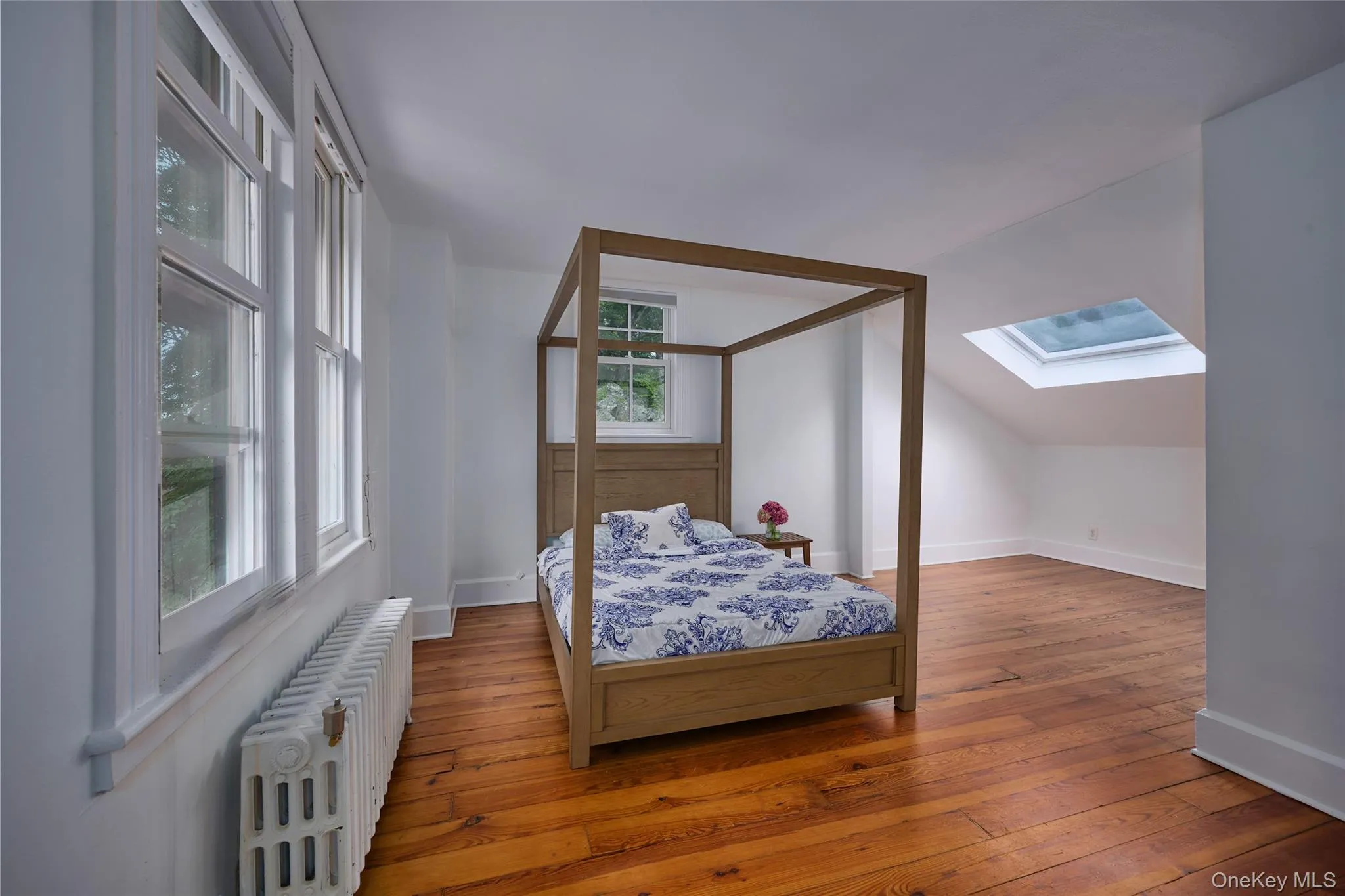 Bedroom with radiator heating unit, hardwood / wood-style floors, vaulted ceiling, and a skylight Bedroom with radiator heating unit, hardwood / wood-style floors, vaulted ceiling, and a skylight