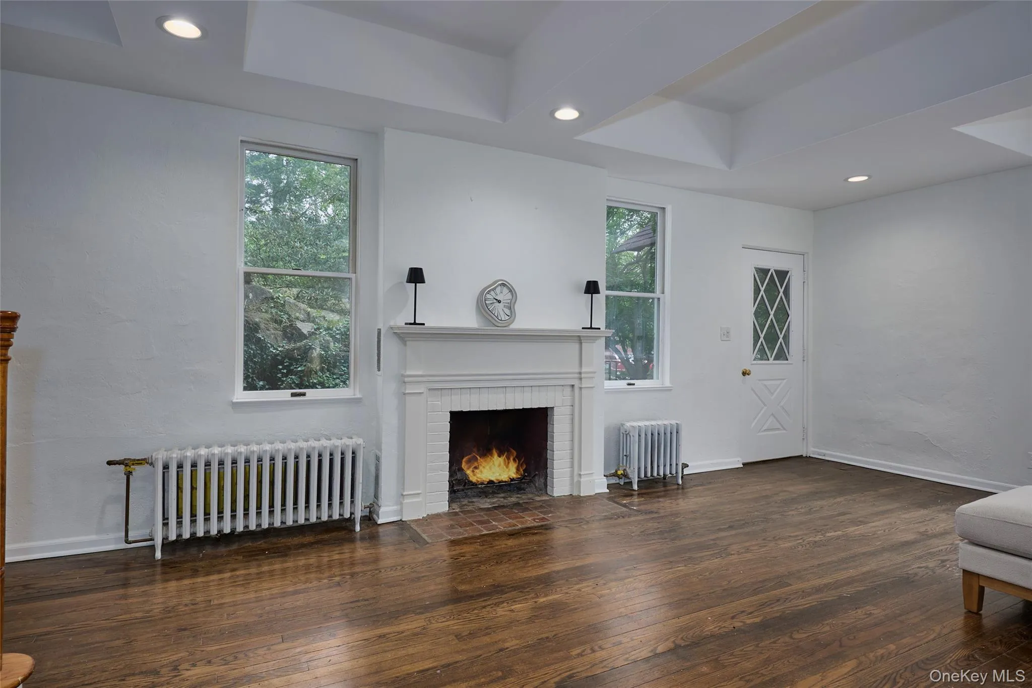 Unfurnished living room featuring radiator, dark wood finished floors, recessed lighting, and a tray ceiling Unfurnished living room featuring radiator, dark wood finished floors, recessed lighting, and a tray ceiling