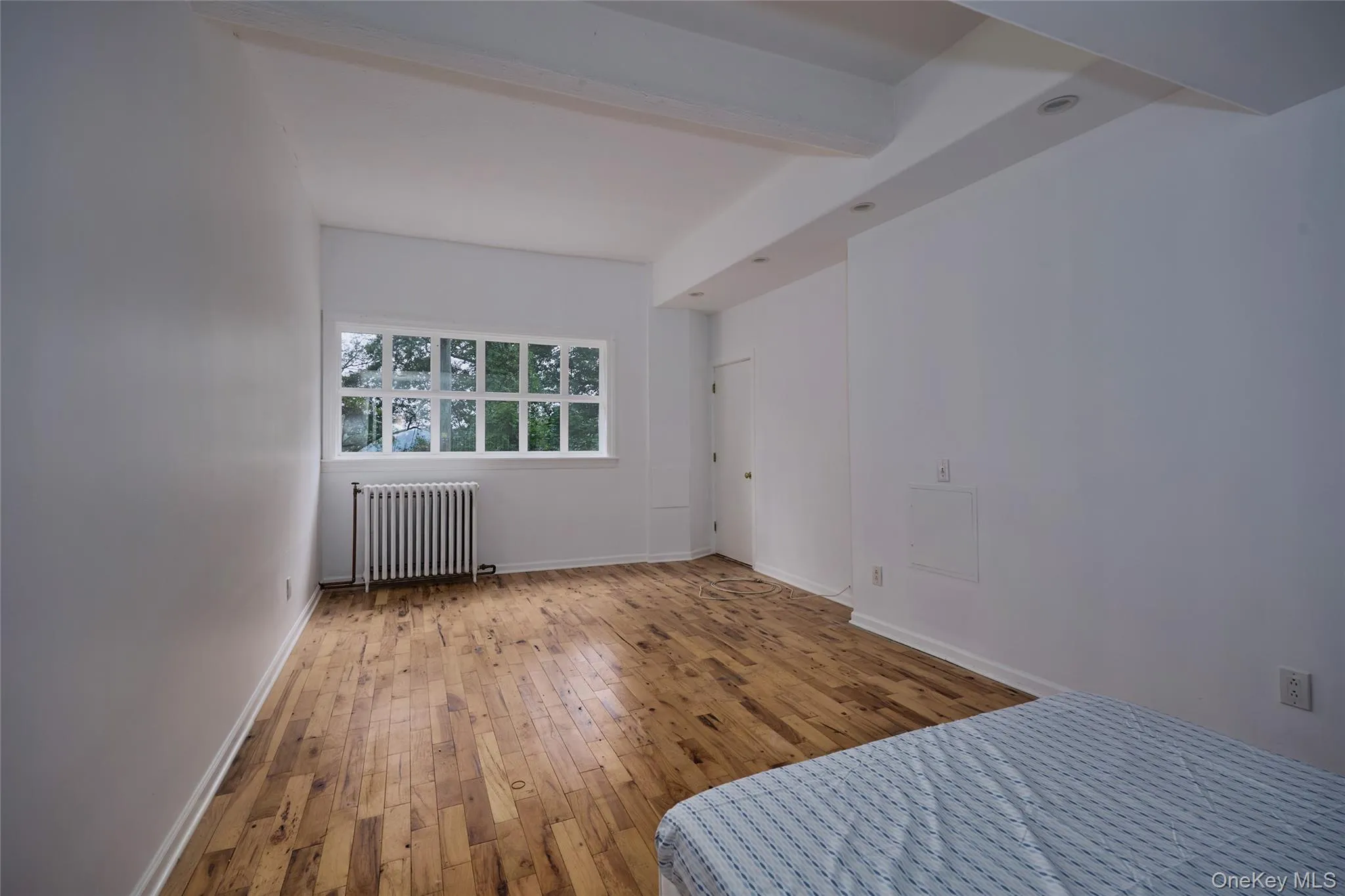 Unfurnished bedroom with beamed ceiling, hardwood / wood-style floors, and radiator heating unit Unfurnished bedroom with beamed ceiling, hardwood / wood-style floors, and radiator heating unit