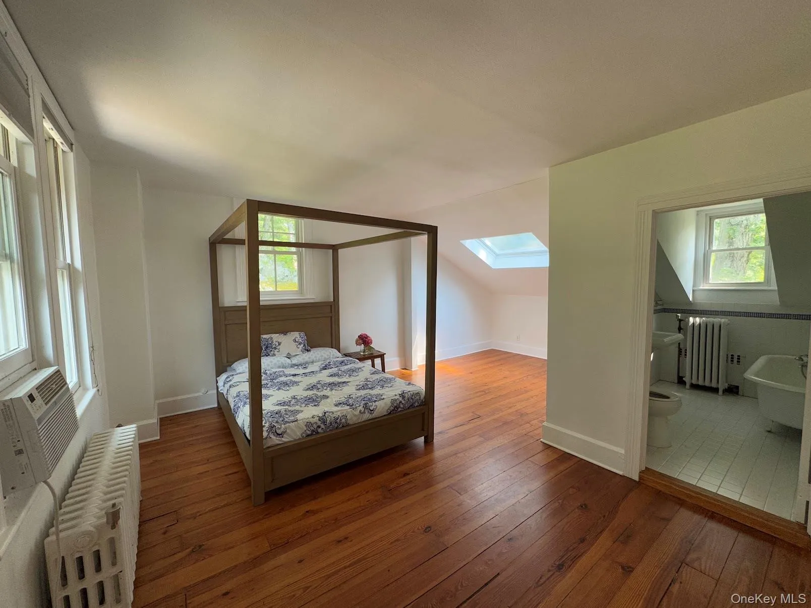 Bedroom with radiator heating unit, hardwood / wood-style floors, a skylight, lofted ceiling, and ensuite bathroom Bedroom with radiator heating unit, hardwood / wood-style floors, a skylight, lofted ceiling, and ensuite bathroom