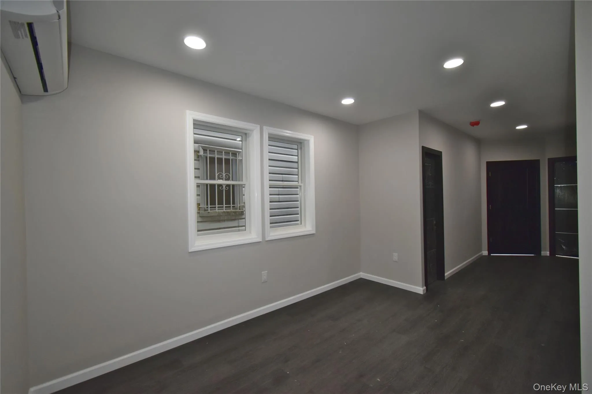Empty room with recessed lighting, dark wood-style flooring, and a wall mounted air conditioner Empty room with recessed lighting, dark wood-style flooring, and a wall mounted air conditioner