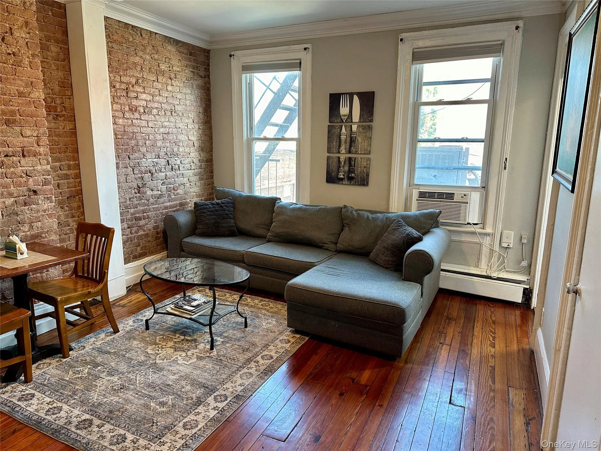 Living area with brick wall, ornamental molding, dark wood-style floors, and a baseboard heating unit Living area with brick wall, ornamental molding, dark wood-style floors, and a baseboard heating unit