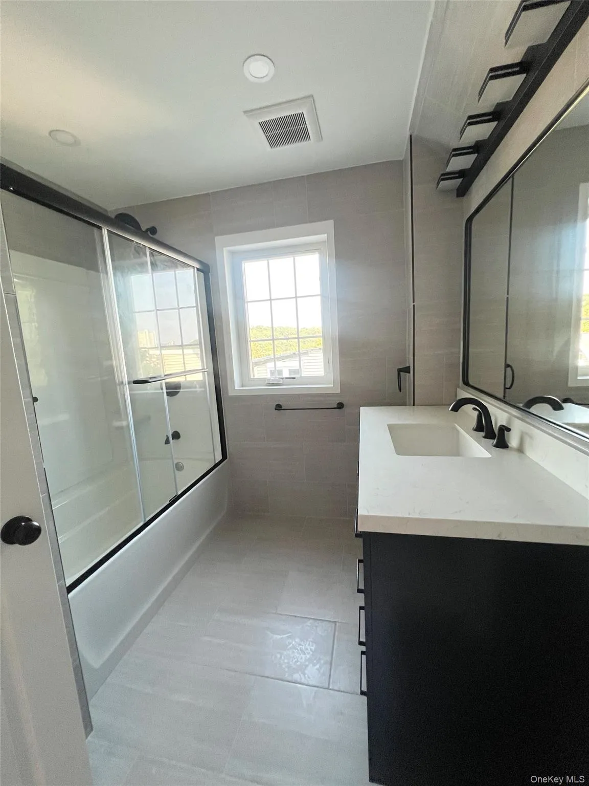 Bathroom featuring combined bath / shower with glass door, tile walls, vanity, and light tile patterned flooring Bathroom featuring combined bath / shower with glass door, tile walls, vanity, and light tile patterned flooring