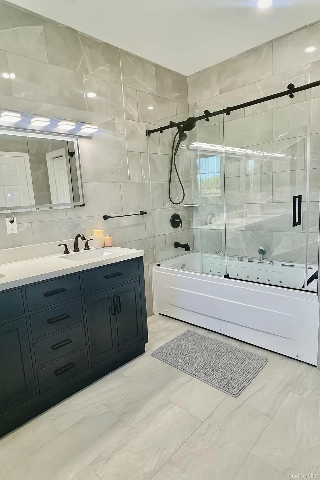 Full bath featuring tile walls, shower / bath combination with glass door, vanity, and tasteful backsplash Full bath featuring tile walls, shower / bath combination with glass door, vanity, and tasteful backsplash