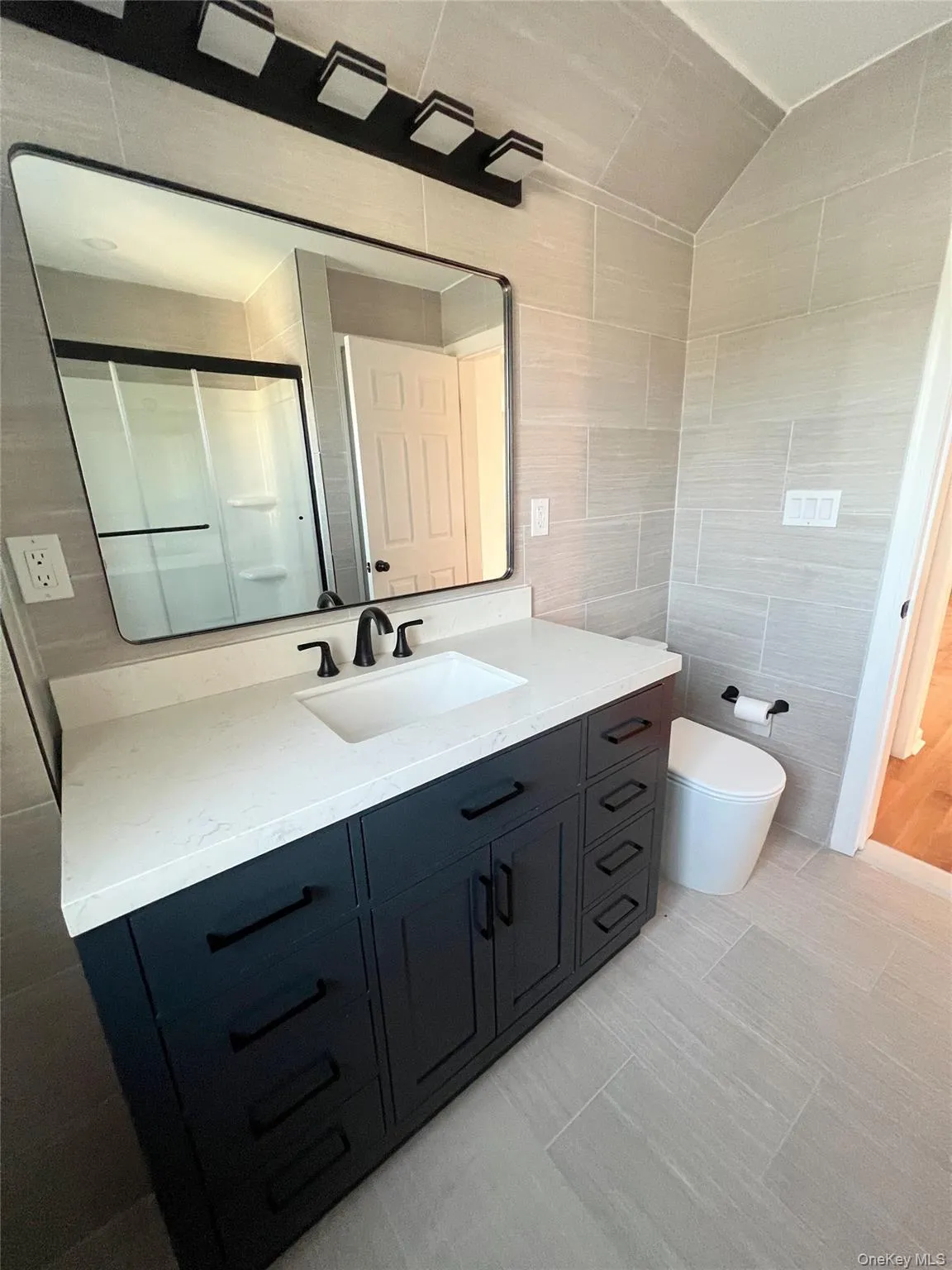 Bathroom featuring tile walls, vanity, a stall shower, and light tile patterned floors Bathroom featuring tile walls, vanity, a stall shower, and light tile patterned floors