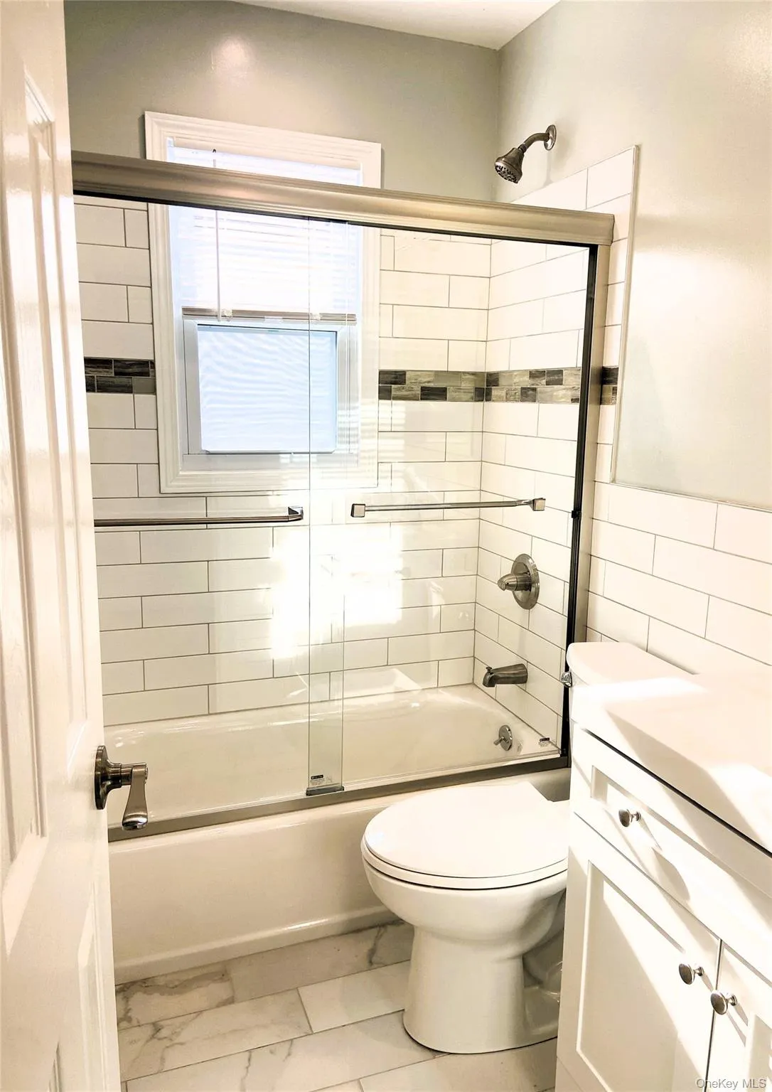 Full bath featuring bath / shower combo with glass door, vanity, marble look tile flooring, and tile walls Full bath featuring bath / shower combo with glass door, vanity, marble look tile flooring, and tile walls