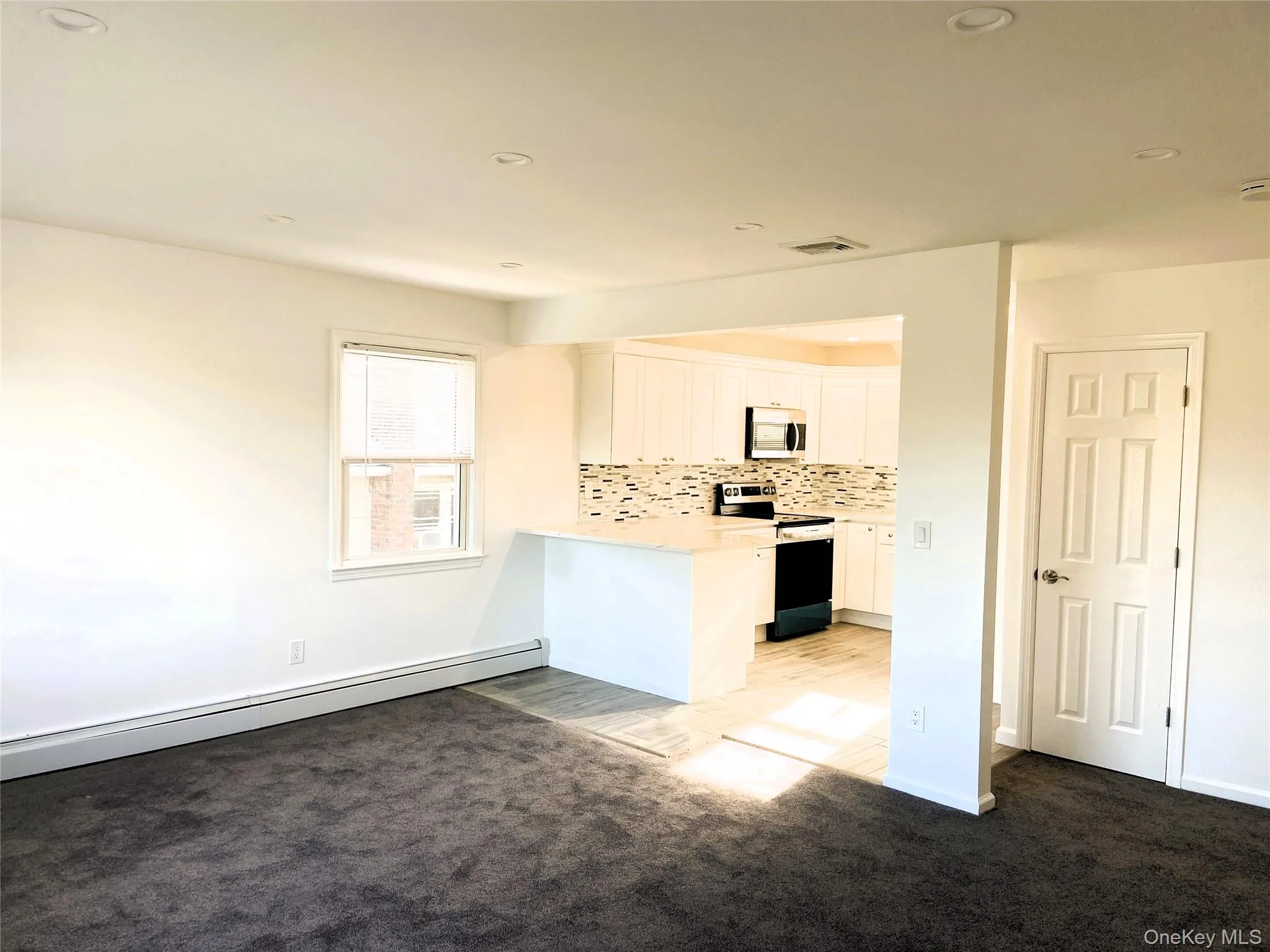 Kitchen with decorative backsplash, a peninsula, stainless steel appliances, white cabinets, and a baseboard radiator Kitchen with decorative backsplash, a peninsula, stainless steel appliances, white cabinets, and a baseboard radiator