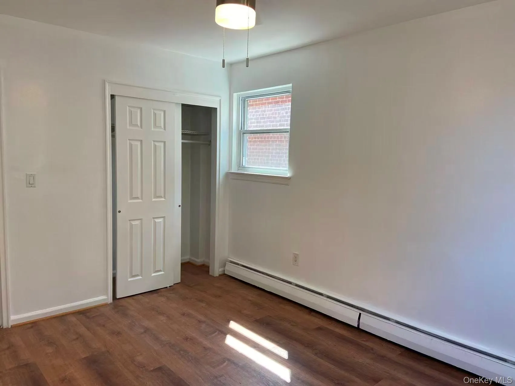 Unfurnished bedroom featuring baseboard heating, dark wood-style flooring, and a closet Unfurnished bedroom featuring baseboard heating, dark wood-style flooring, and a closet