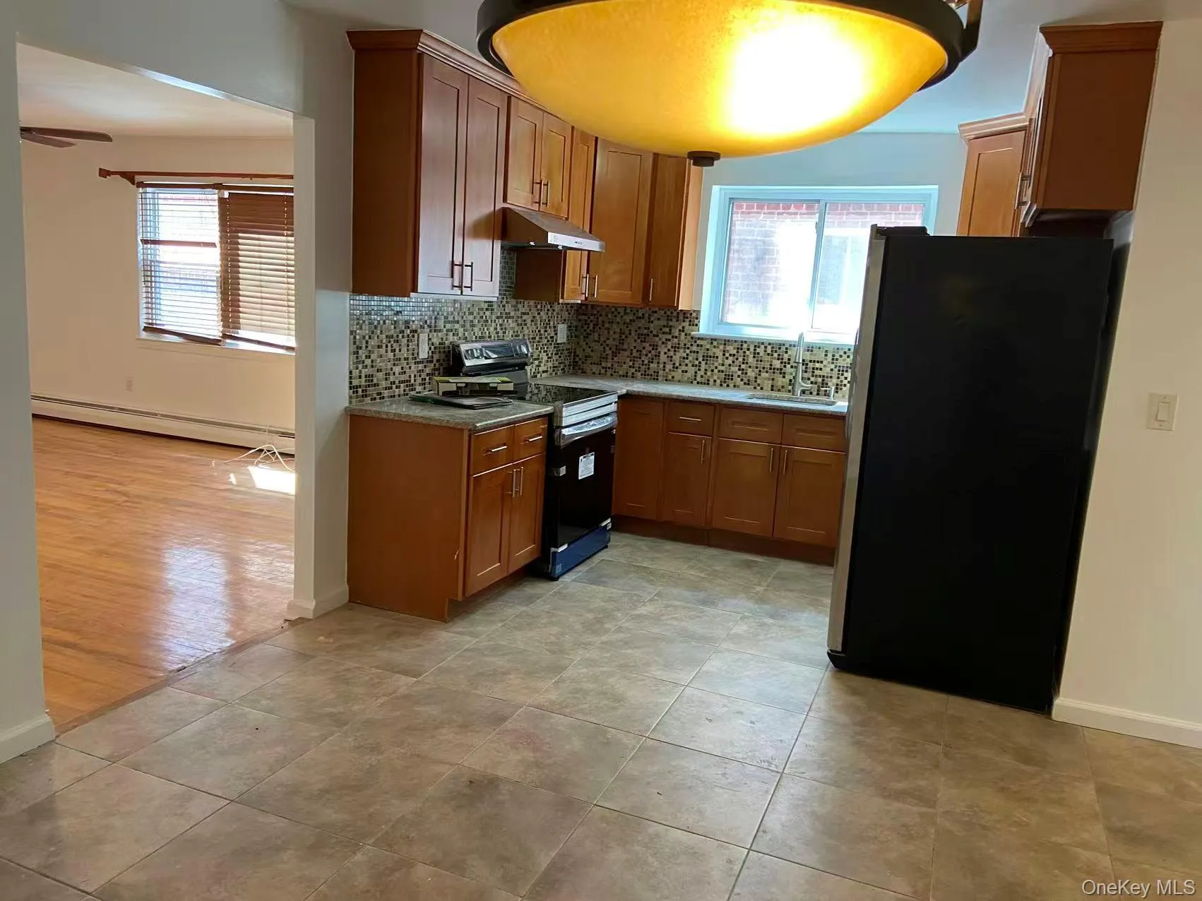 Kitchen with backsplash, stainless steel appliances, brown cabinetry, and a baseboard radiator Kitchen with backsplash, stainless steel appliances, brown cabinetry, and a baseboard radiator