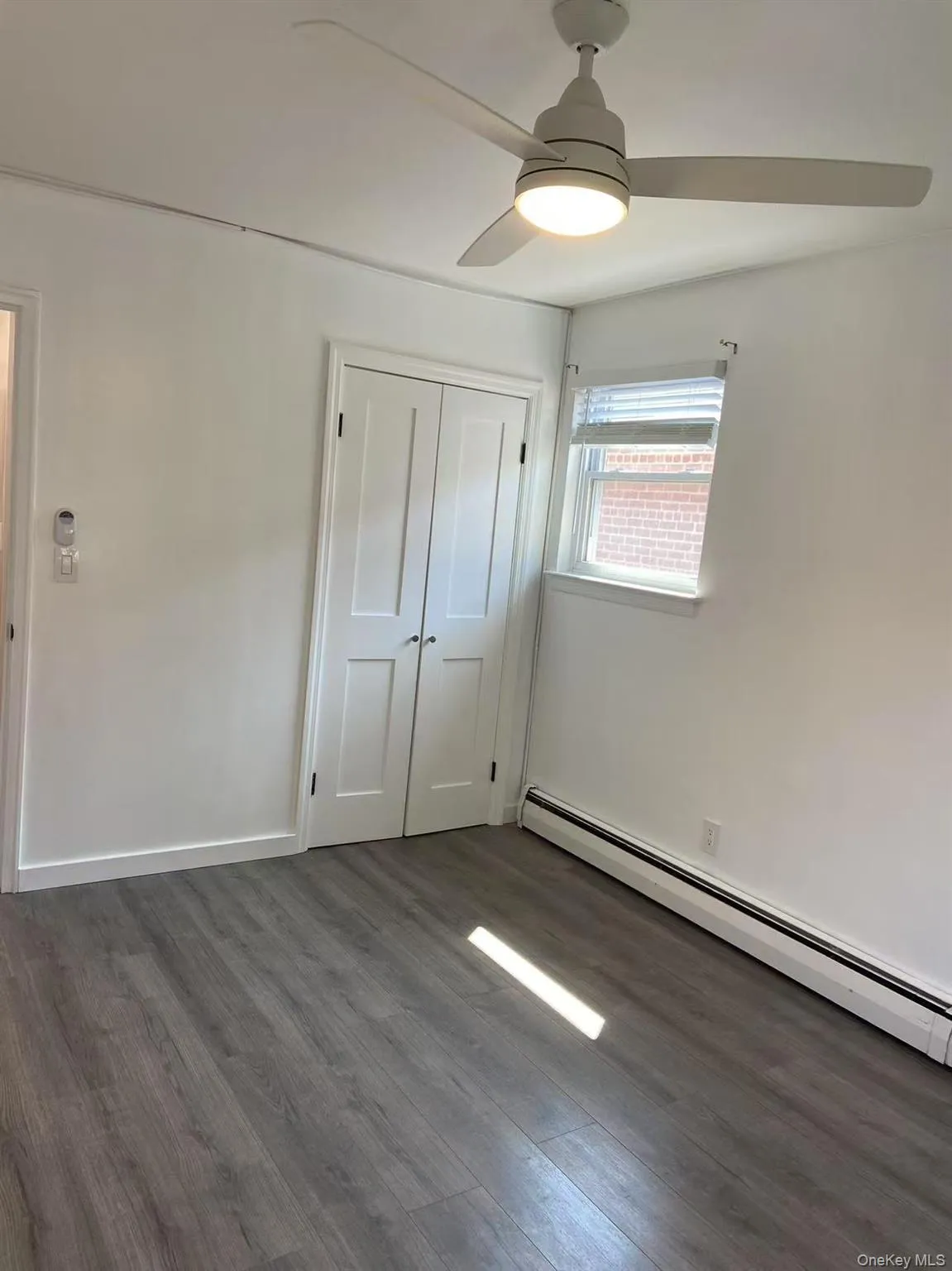 Unfurnished bedroom with a baseboard radiator, dark wood-style flooring, a closet, and a ceiling fan Unfurnished bedroom with a baseboard radiator, dark wood-style flooring, a closet, and a ceiling fan