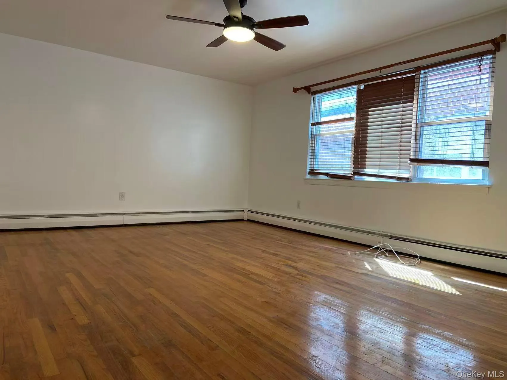 Empty room featuring hardwood / wood-style flooring, baseboard heating, and ceiling fan Empty room featuring hardwood / wood-style flooring, baseboard heating, and ceiling fan