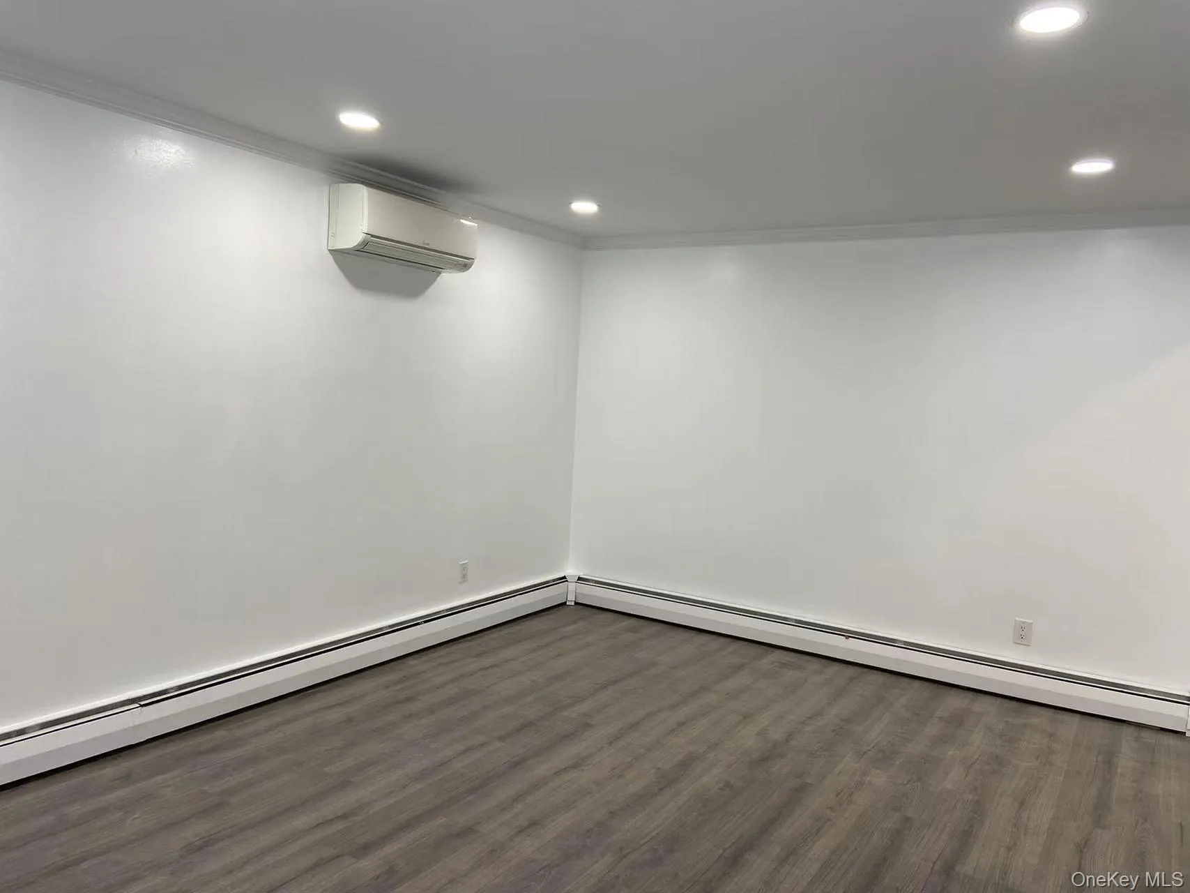 Basement featuring dark wood finished floors, a wall mounted AC, crown molding, recessed lighting, and a baseboard heating unit Basement featuring dark wood finished floors, a wall mounted AC, crown molding, recessed lighting, and a baseboard heating unit