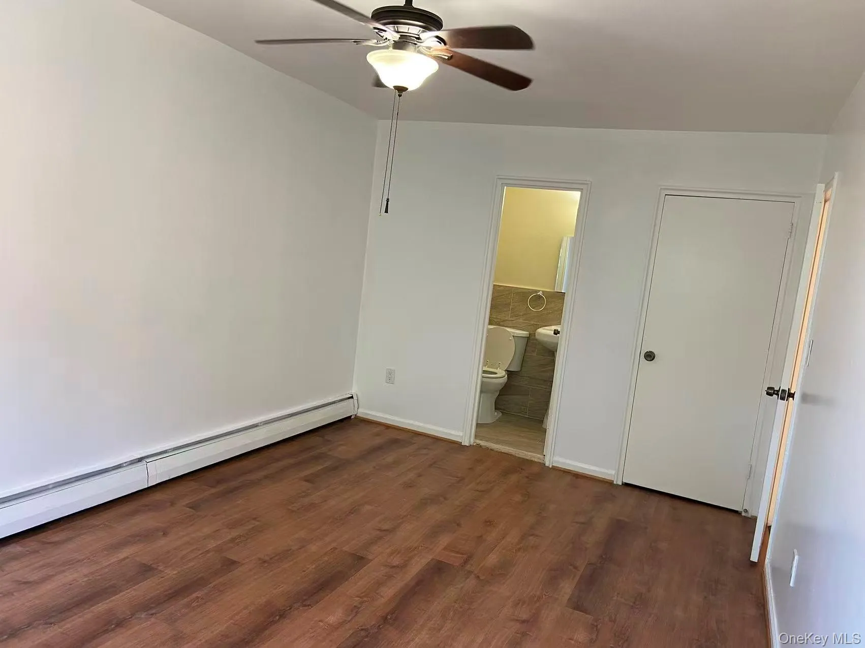 Unfurnished bedroom featuring dark wood-type flooring, a baseboard radiator, a ceiling fan, and ensuite bathroom Unfurnished bedroom featuring dark wood-type flooring, a baseboard radiator, a ceiling fan, and ensuite bathroom