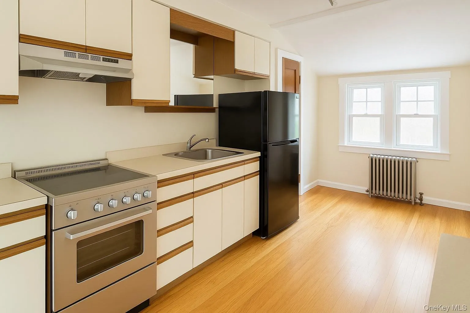 Kitchen with stainless steel electric range oven, under cabinet range hood, radiator, freestanding refrigerator, and white cabinets Kitchen with stainless steel electric range oven, under cabinet range hood, radiator, freestanding refrigerator, and white cabinets