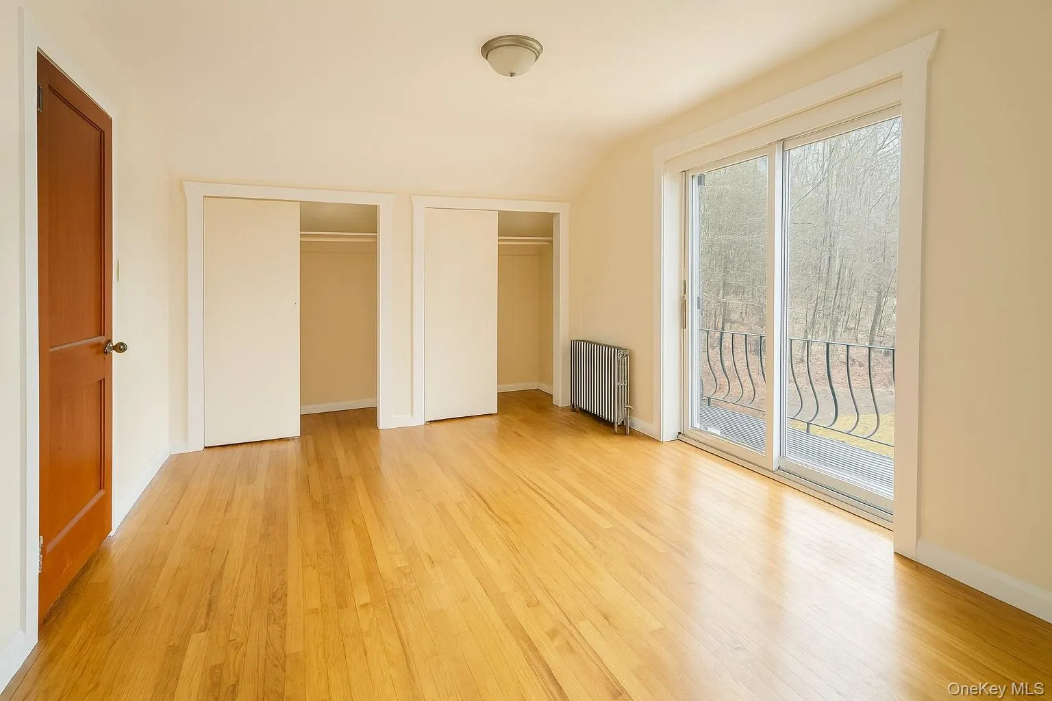 Unfurnished bedroom featuring multiple closets, access to outside, radiator heating unit, and light wood-style flooring Unfurnished bedroom featuring multiple closets, access to outside, radiator heating unit, and light wood-style flooring