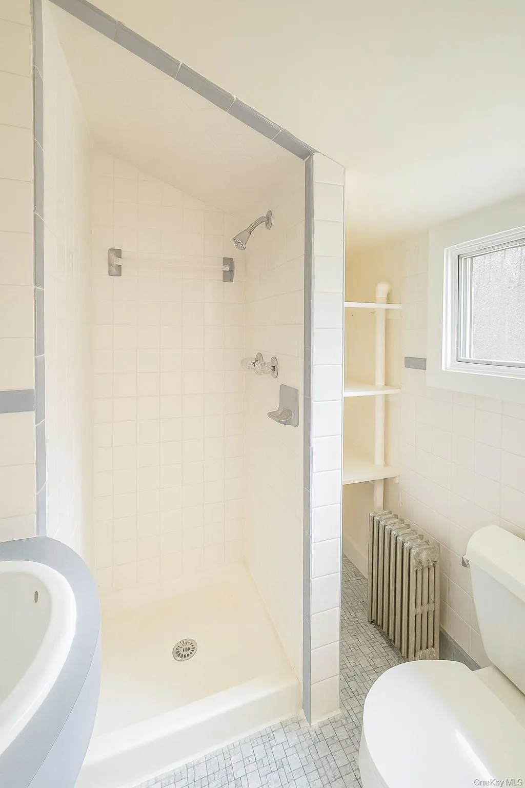 Full bath featuring radiator heating unit, tile patterned flooring, a stall shower, and tile walls Full bath featuring radiator heating unit, tile patterned flooring, a stall shower, and tile walls