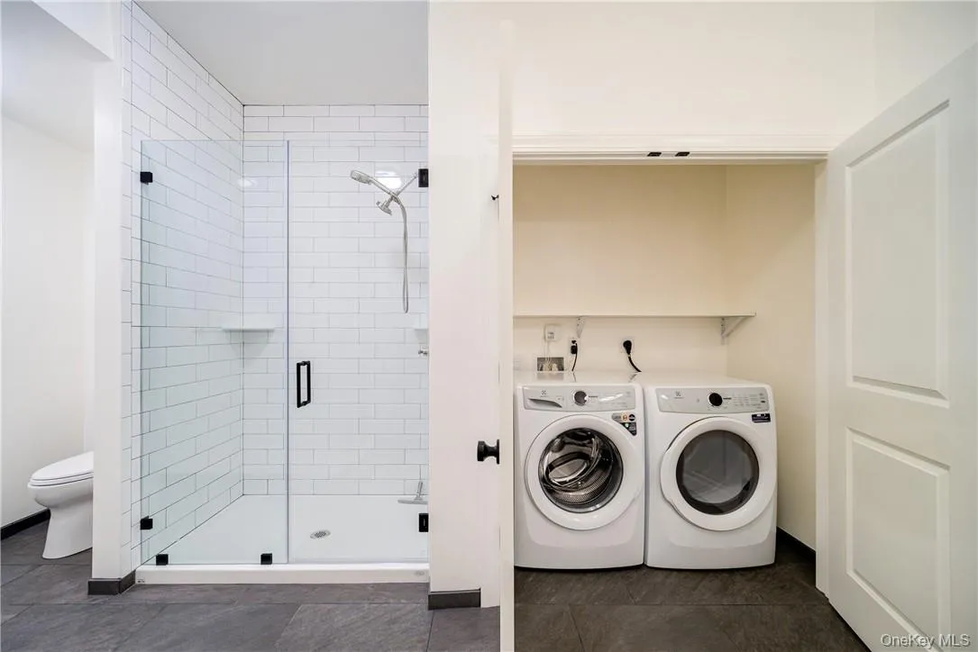 Washroom with electric dryer hookup, washer and clothes dryer, and dark tile flooring Washroom with electric dryer hookup, washer and clothes dryer, and dark tile flooring