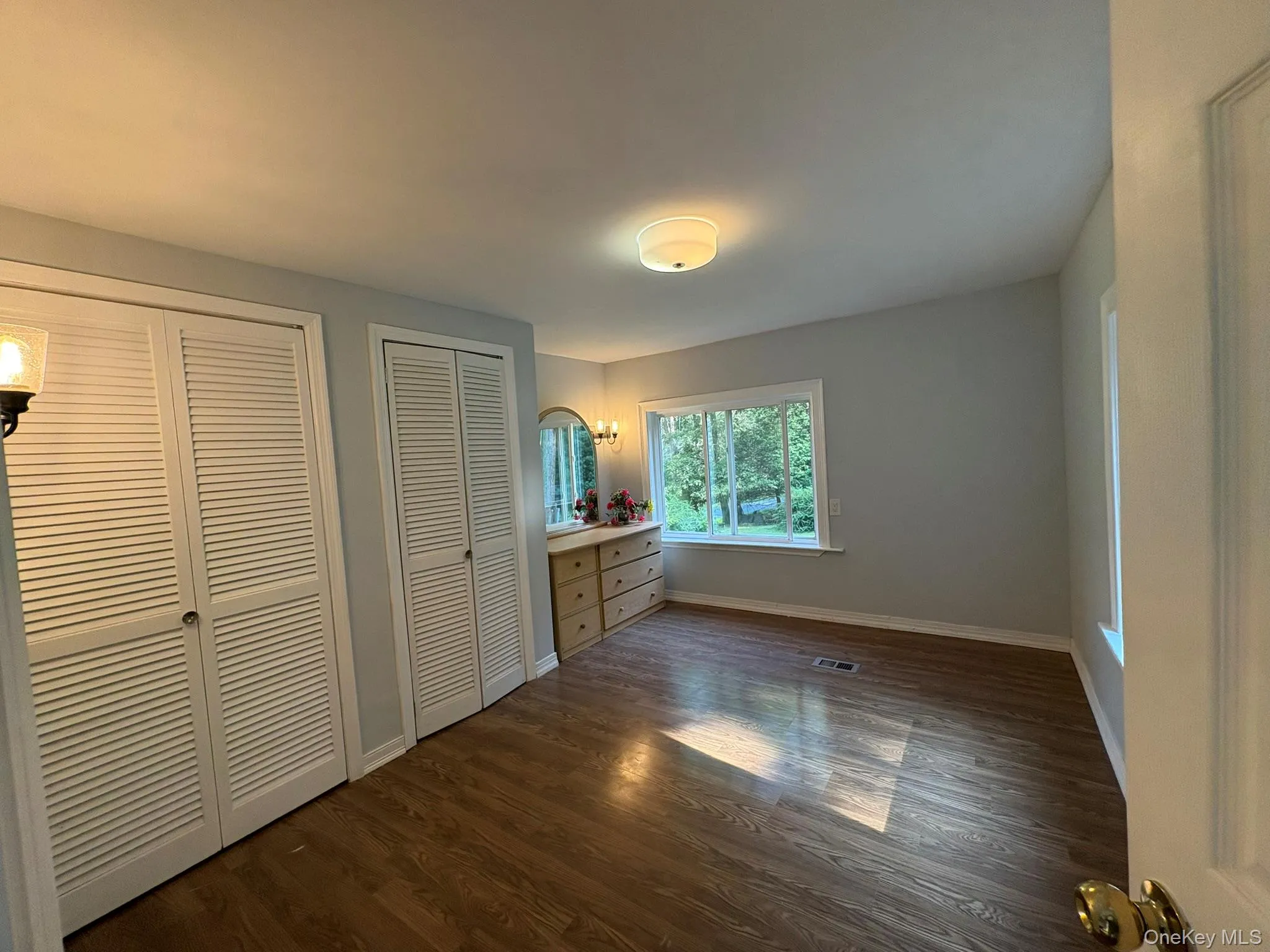Unfurnished bedroom featuring multiple closets and dark wood-style flooring Unfurnished bedroom featuring multiple closets and dark wood-style flooring