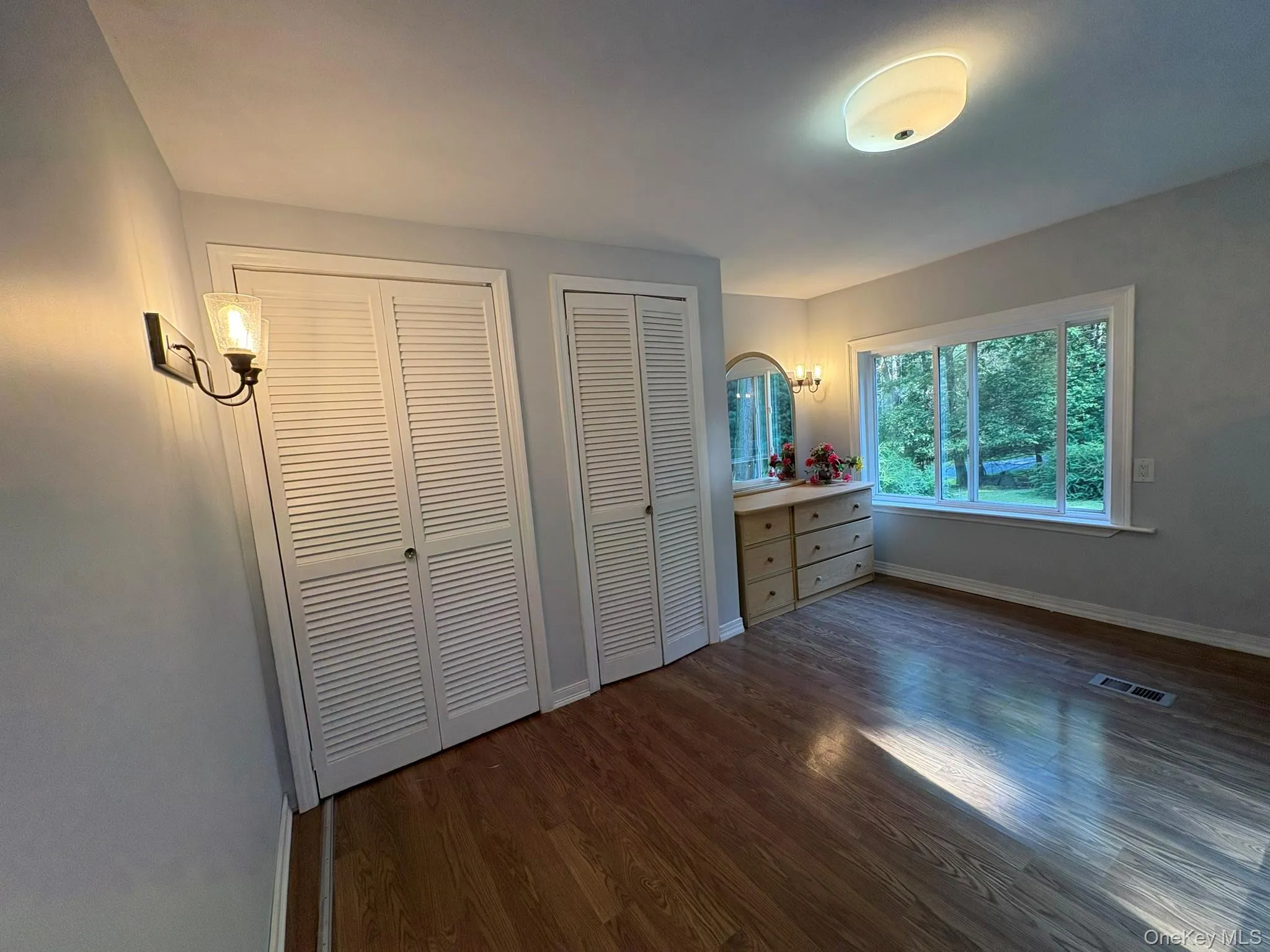 Unfurnished bedroom featuring two closets and dark wood-style floors Unfurnished bedroom featuring two closets and dark wood-style floors