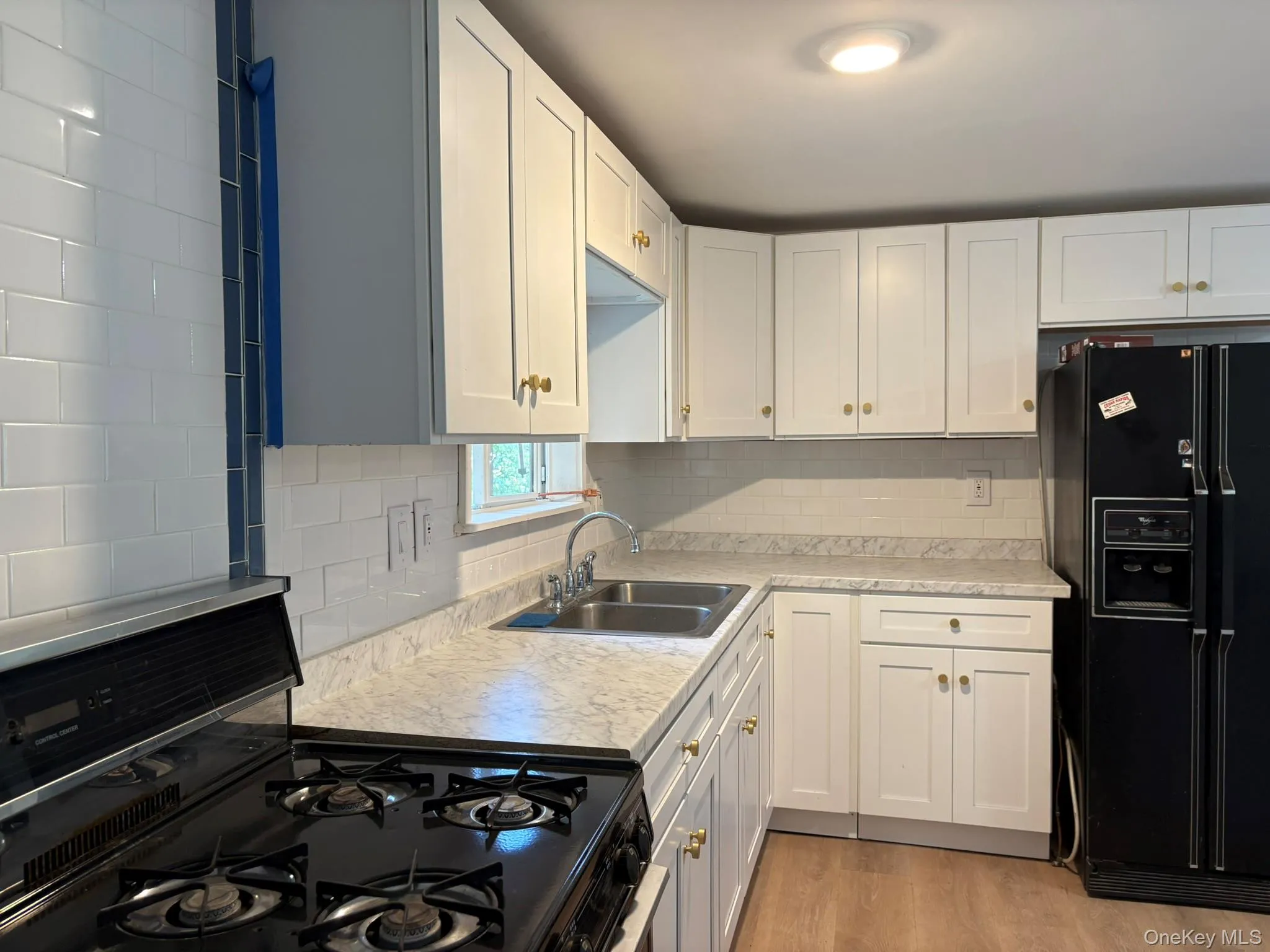 Kitchen featuring black appliances, light countertops, white cabinets, tasteful backsplash, and light wood-style flooring Kitchen featuring black appliances, light countertops, white cabinets, tasteful backsplash, and light wood-style flooring