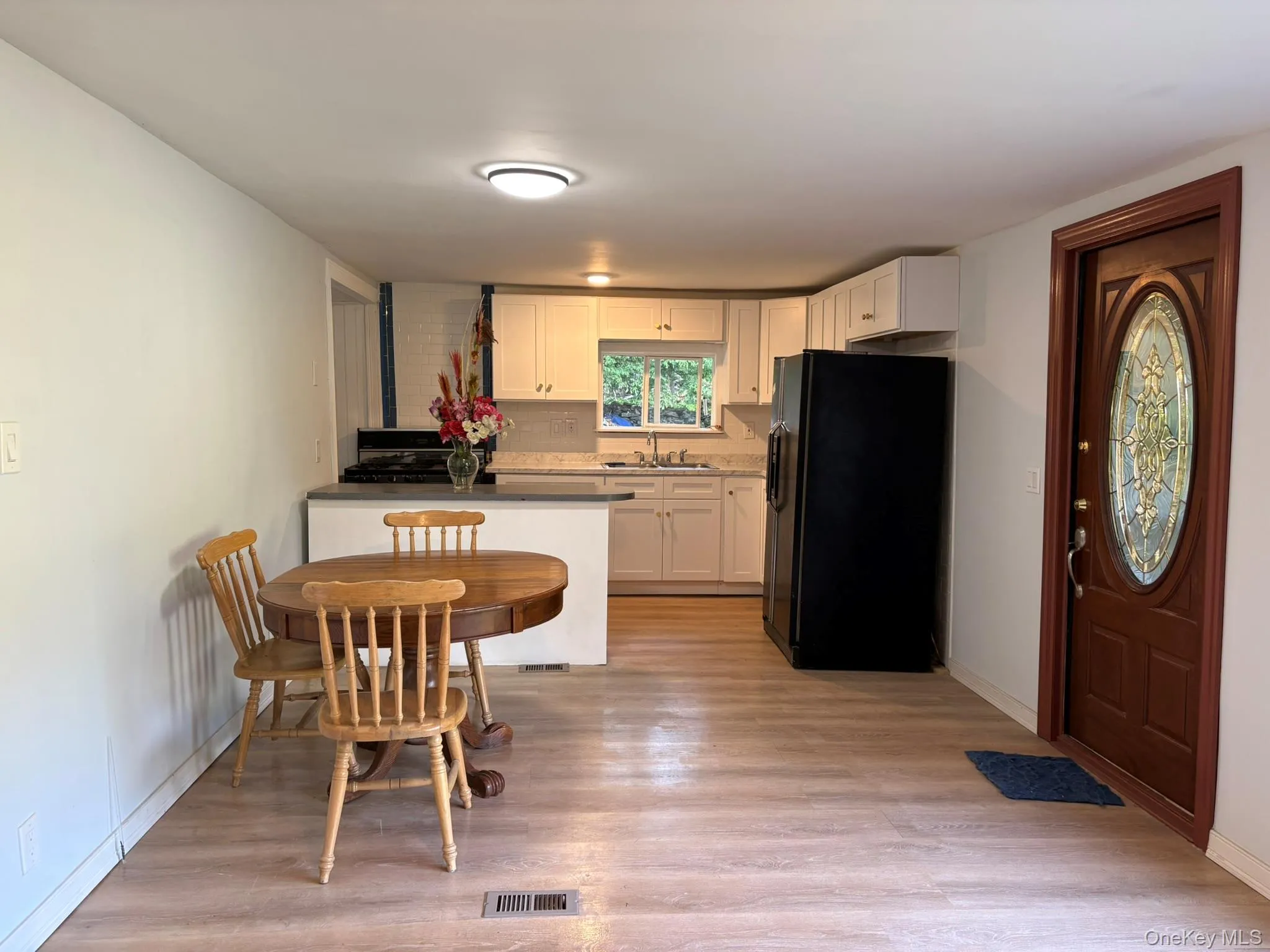 Kitchen with black fridge, white cabinets, light wood finished floors, and tasteful backsplash Kitchen with black fridge, white cabinets, light wood finished floors, and tasteful backsplash