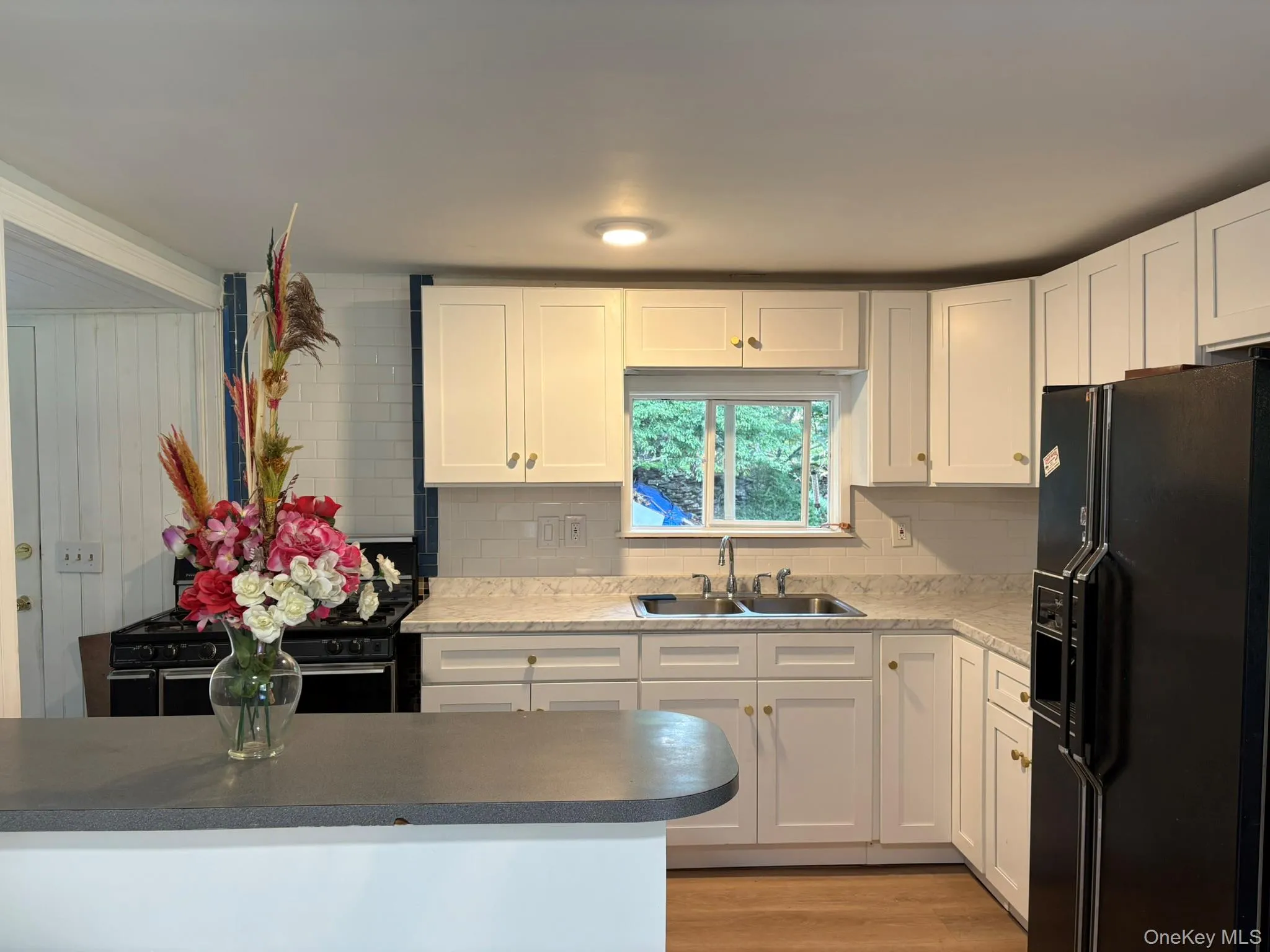 Kitchen with black appliances, white cabinets, tasteful backsplash, and light wood-type flooring Kitchen with black appliances, white cabinets, tasteful backsplash, and light wood-type flooring