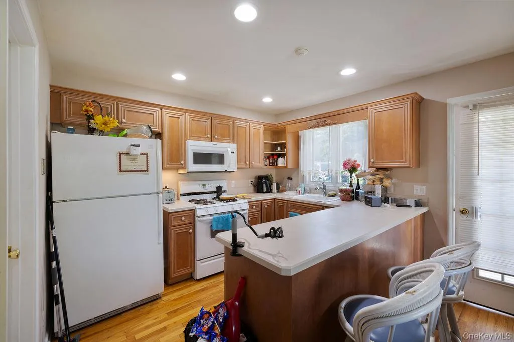 Kitchen featuring white appliances, light countertops, light wood-style floors, open shelves, and a peninsula Kitchen featuring white appliances, light countertops, light wood-style floors, open shelves, and a peninsula