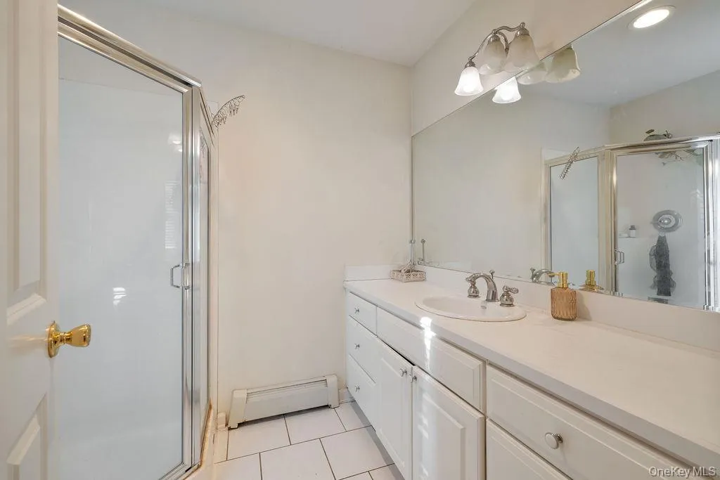 Full bathroom with light tile patterned flooring, a baseboard radiator, vanity, a shower stall, and recessed lighting Full bathroom with light tile patterned flooring, a baseboard radiator, vanity, a shower stall, and recessed lighting