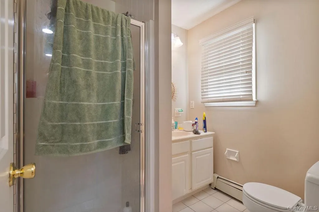 Full bath with light tile patterned floors, vanity, a baseboard radiator, and a stall shower Full bath with light tile patterned floors, vanity, a baseboard radiator, and a stall shower