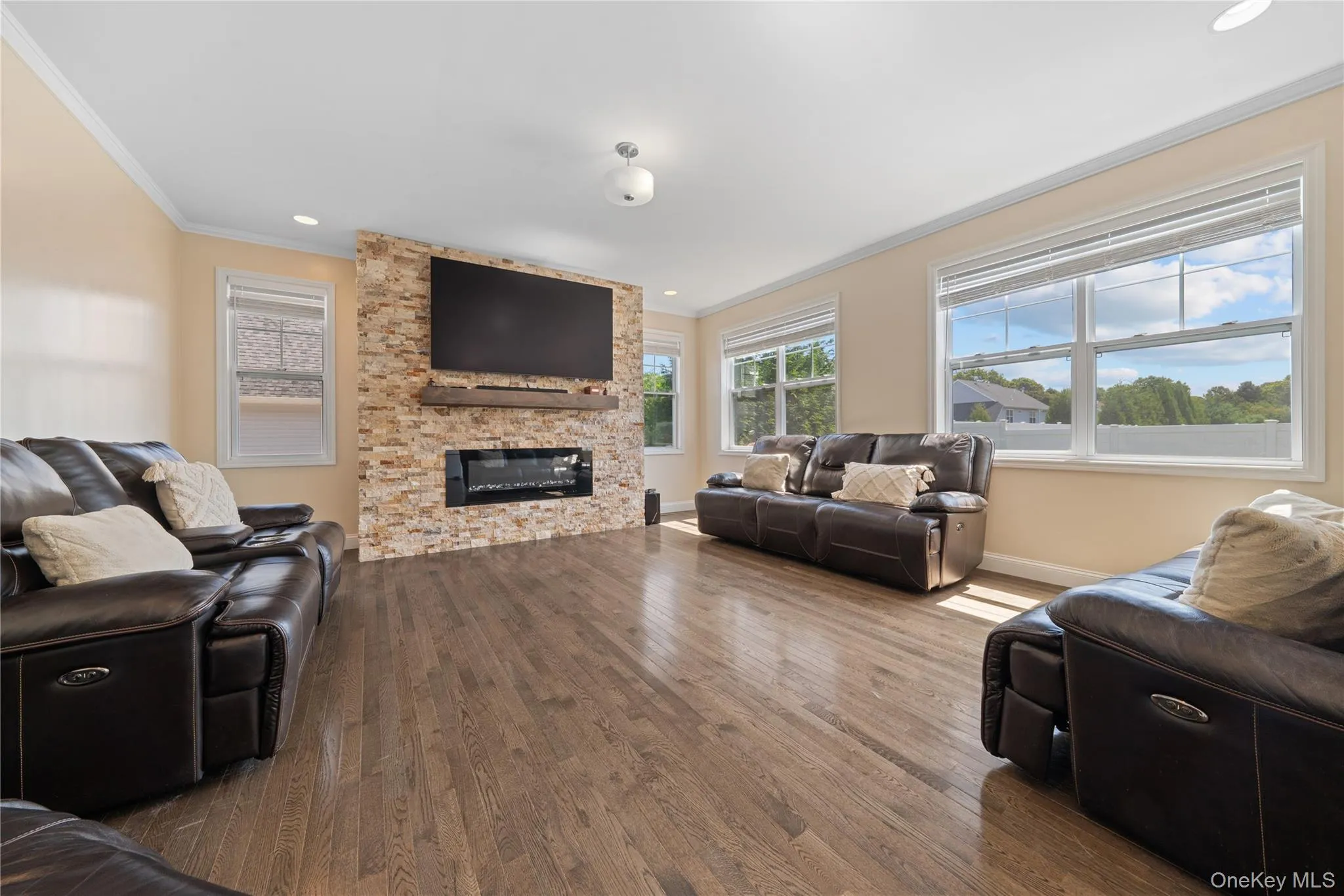 Living room with ornamental molding, wood finished floors, plenty of natural light, a stone fireplace, and recessed lighting Living room with ornamental molding, wood finished floors, plenty of natural light, a stone fireplace, and recessed lighting
