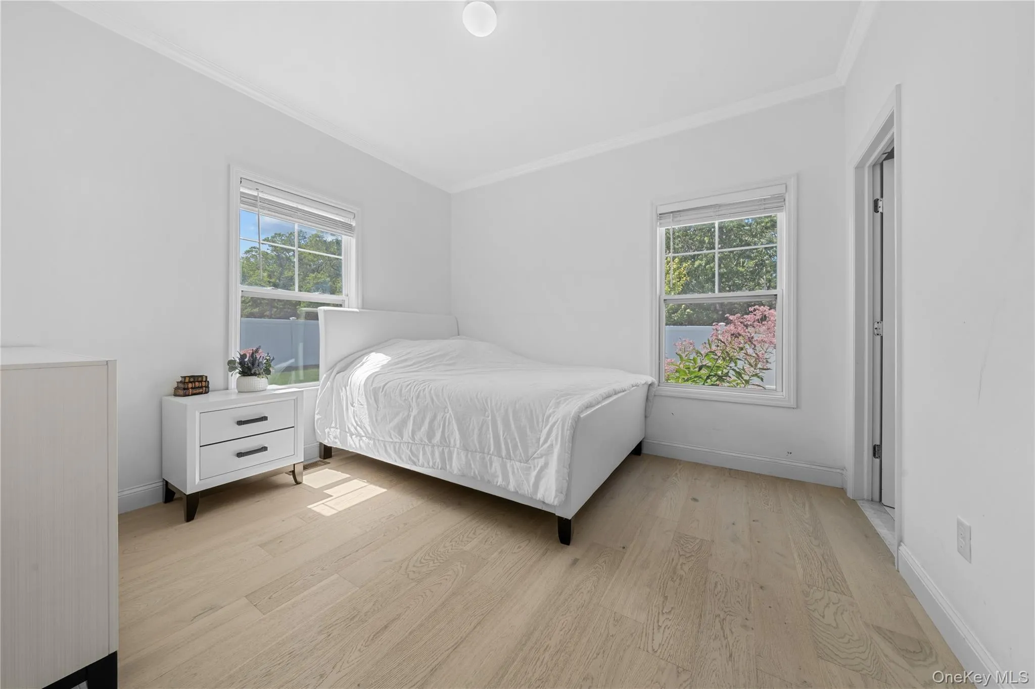 Bedroom with light wood finished floors, crown molding, and multiple windows Bedroom with light wood finished floors, crown molding, and multiple windows