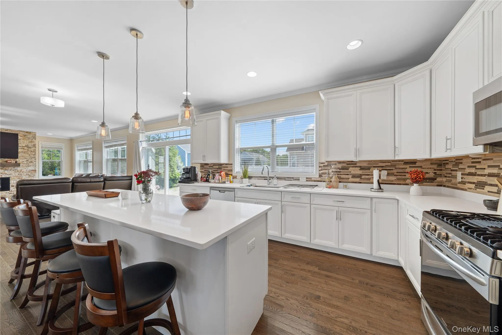 Kitchen with open floor plan, hanging light fixtures, white cabinets, tasteful backsplash, and ornamental molding Kitchen with open floor plan, hanging light fixtures, white cabinets, tasteful backsplash, and ornamental molding