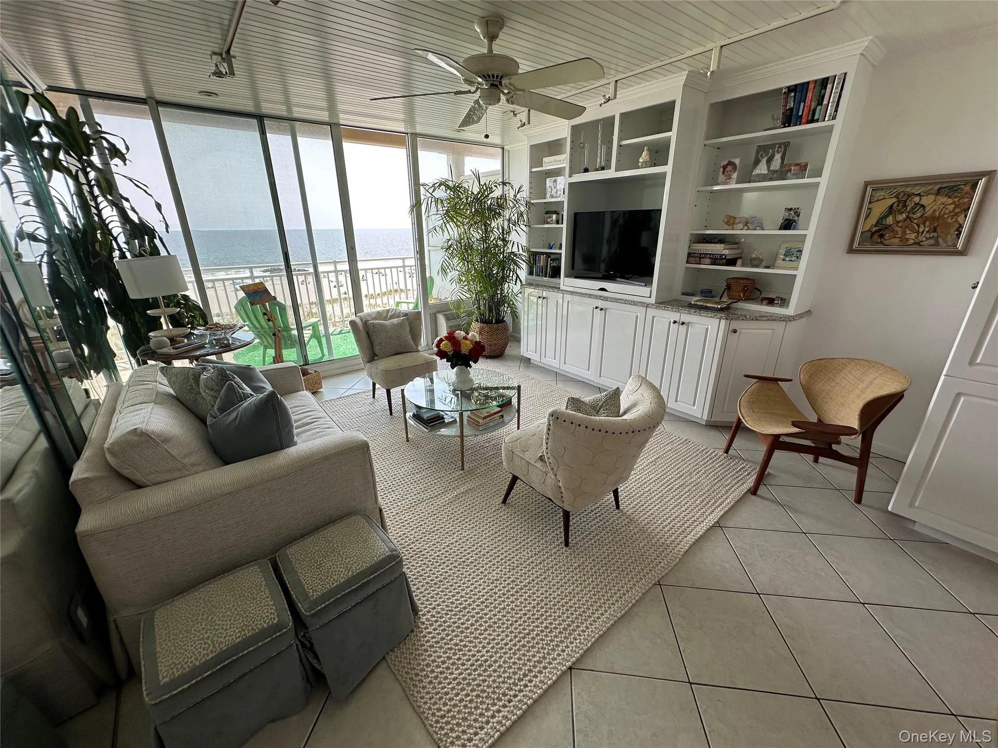 Living room featuring light tile patterned floors, a ceiling fan, a wall of windows, and rail lighting Living room featuring light tile patterned floors, a ceiling fan, a wall of windows, and rail lighting