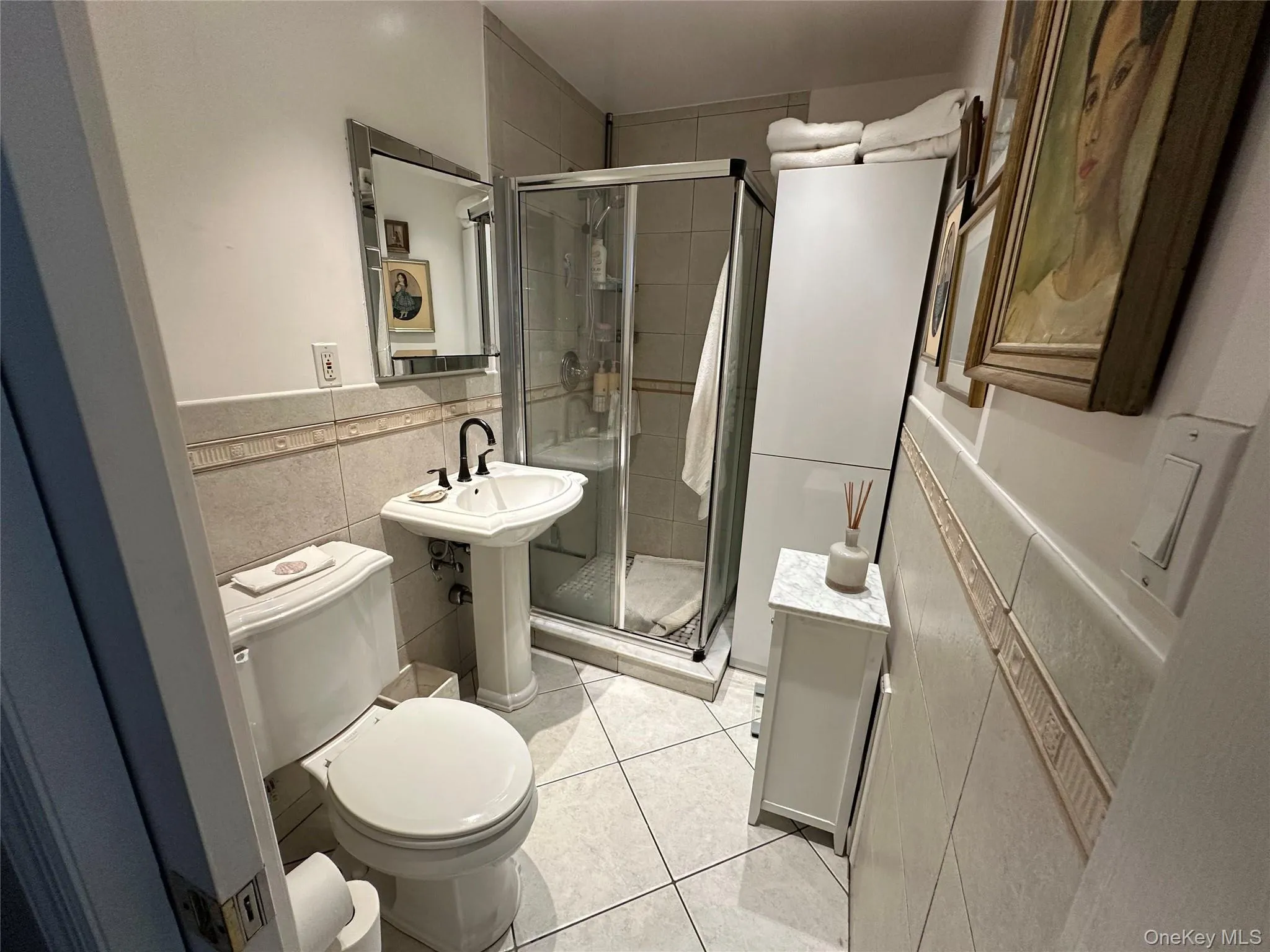 Full bath featuring tile walls, a shower stall, light tile patterned flooring, and wainscoting Full bath featuring tile walls, a shower stall, light tile patterned flooring, and wainscoting