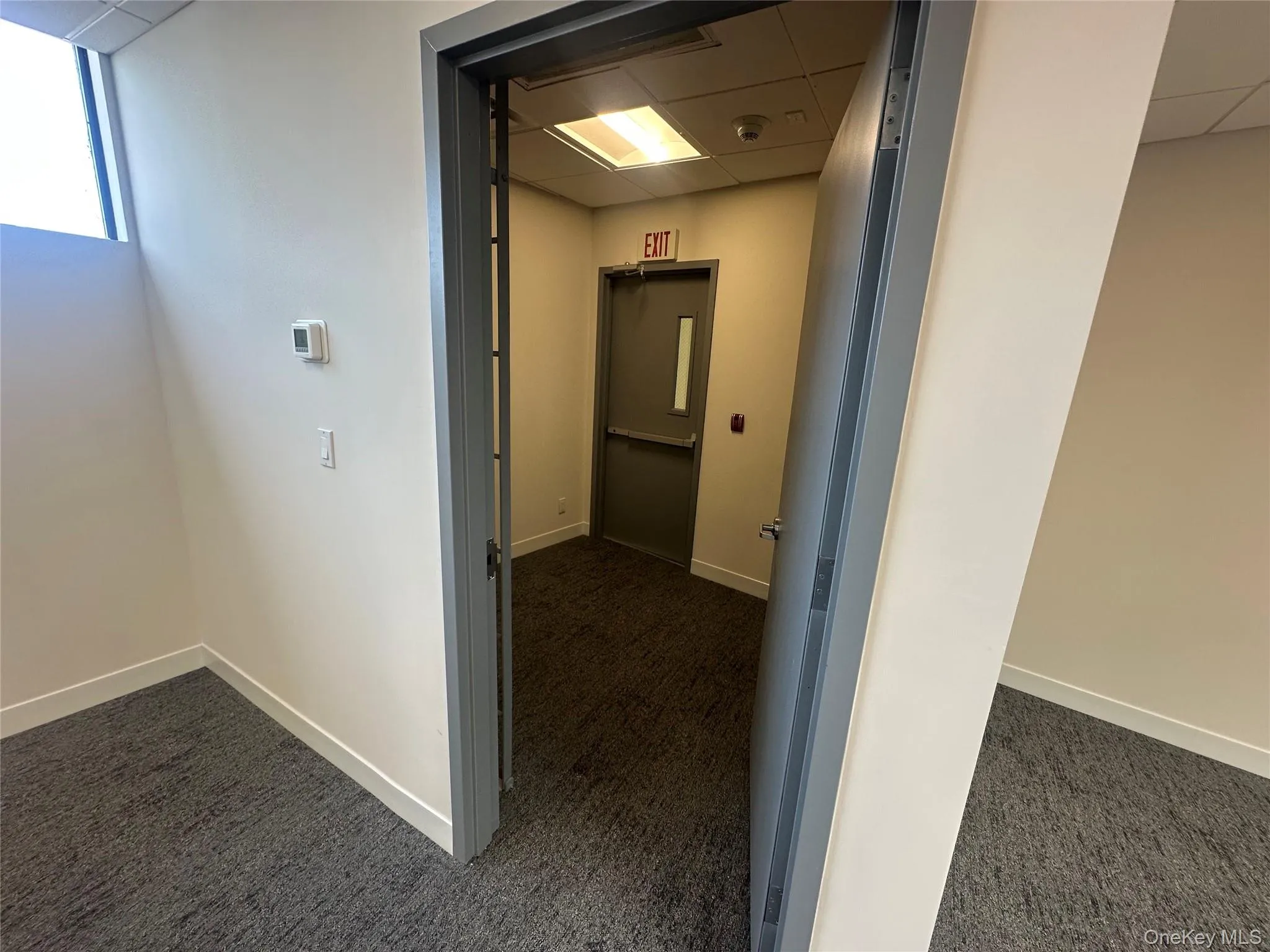 Corridor with a paneled ceiling and dark colored carpet Corridor with a paneled ceiling and dark colored carpet