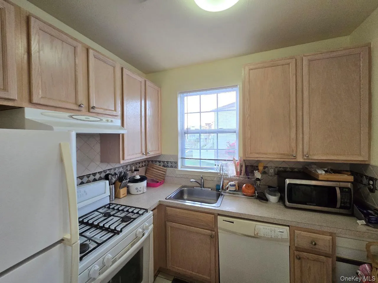 Kitchen with white appliances, light countertops, backsplash, and light brown cabinets Kitchen with white appliances, light countertops, backsplash, and light brown cabinets