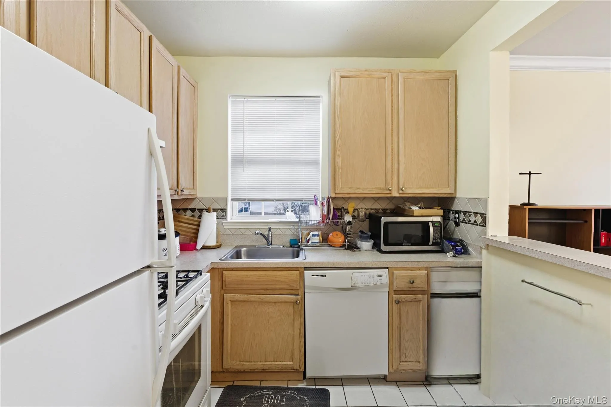 Kitchen featuring white appliances, light brown cabinets, light countertops, light tile patterned flooring, and decorative backsplash Kitchen featuring white appliances, light brown cabinets, light countertops, light tile patterned flooring, and decorative backsplash
