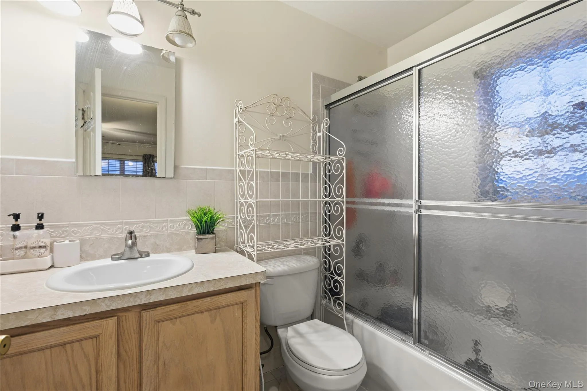 Full bathroom featuring vanity, bath / shower combo with glass door, and tile walls Full bathroom featuring vanity, bath / shower combo with glass door, and tile walls
